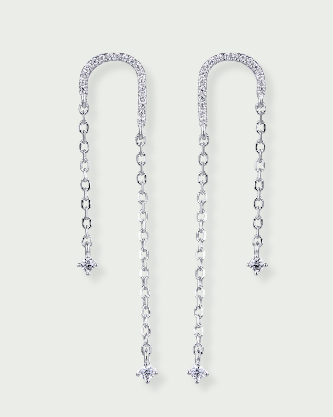 Boucles asymétriques en argent 925 rhodié, arc pavé de zirconiums et fines chaînes terminées par des pendants en pierres blanches.