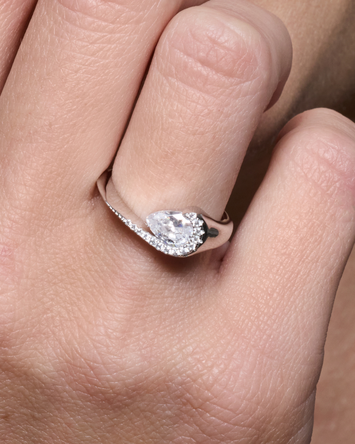 Bague Pear Glow blanche en argent 925 rhodié avec pierre centrale en zirconium taille poire entourée d’un délicat pavage de zirconiums, design fluide et asymétrique qui épouse le doigt pour un éclat subtil et raffiné.