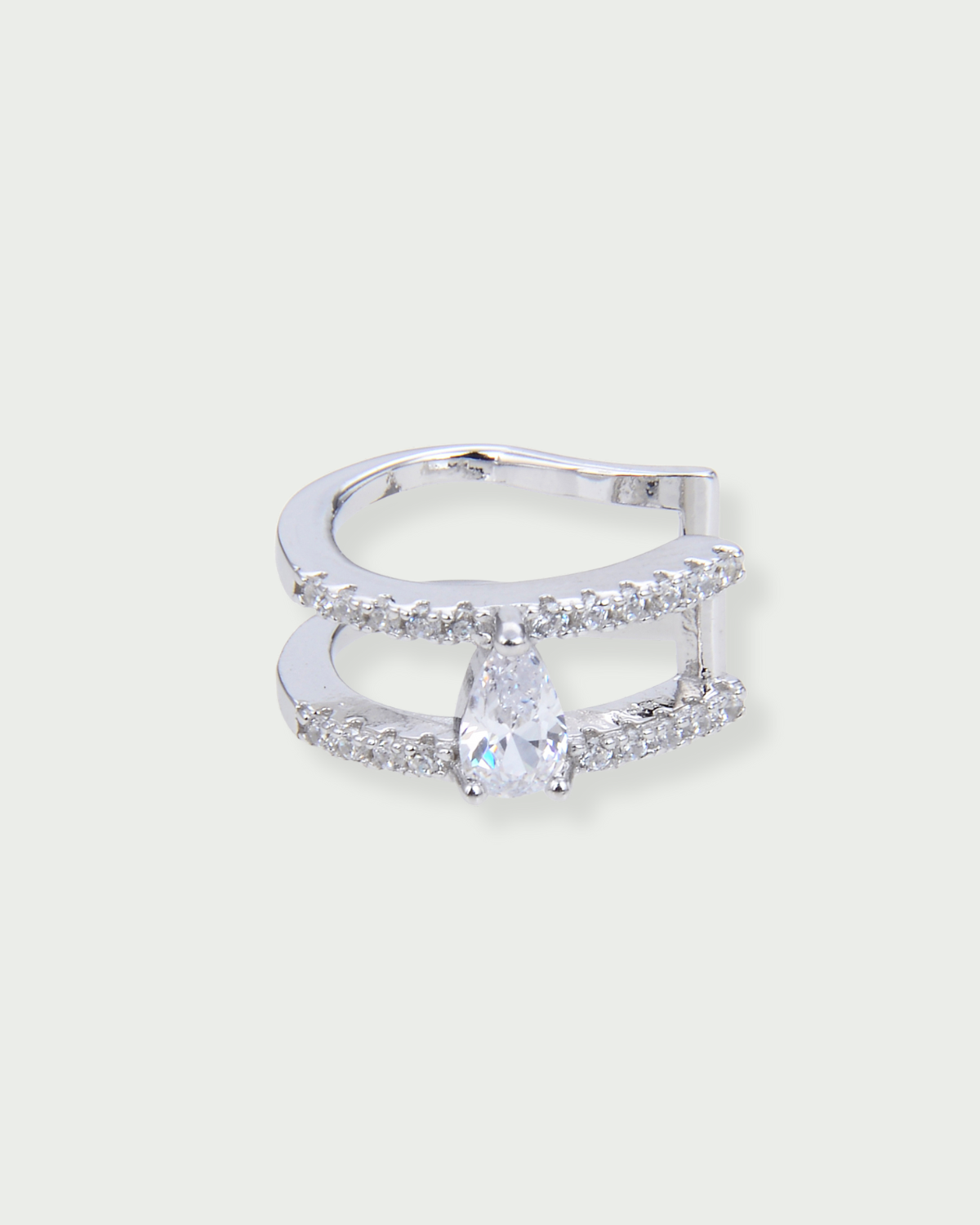 Earcuff Signature blanc en argent 925 rhodié avec double anneau ouvert orné d’un zirconium taille poire et de pavage de pierres, design audacieux et lumineux qui épouse délicatement l’oreille sans perçage, pour une touche moderne et élégante.