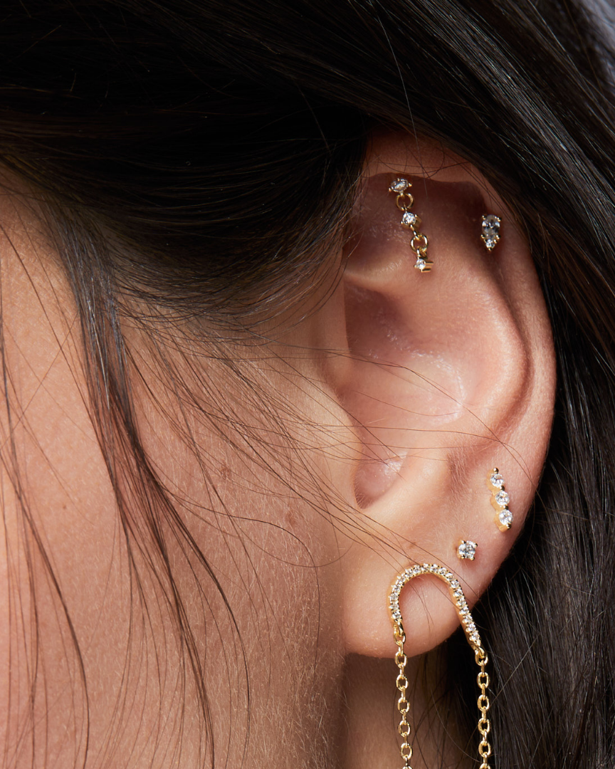 Piercing d’oreille en argent 925 millièmes doré à l’or fin 18 carats, sublimé par trois petites pierres en zirconium délicatement montées sur une fine chaîne. Un design aérien et lumineux qui crée un subtil mouvement à chaque geste.
Longueur 19 mm, tige 8 mm, finition polie brillante.