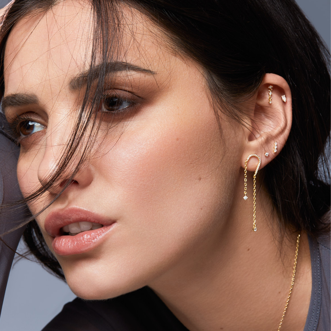 Piercing d’oreille en argent 925 millièmes doré à l’or fin 18 carats, sublimé par trois petites pierres en zirconium délicatement montées sur une fine chaîne. Un design aérien et lumineux qui crée un subtil mouvement à chaque geste.
Longueur 19 mm, tige 8 mm, finition polie brillante.