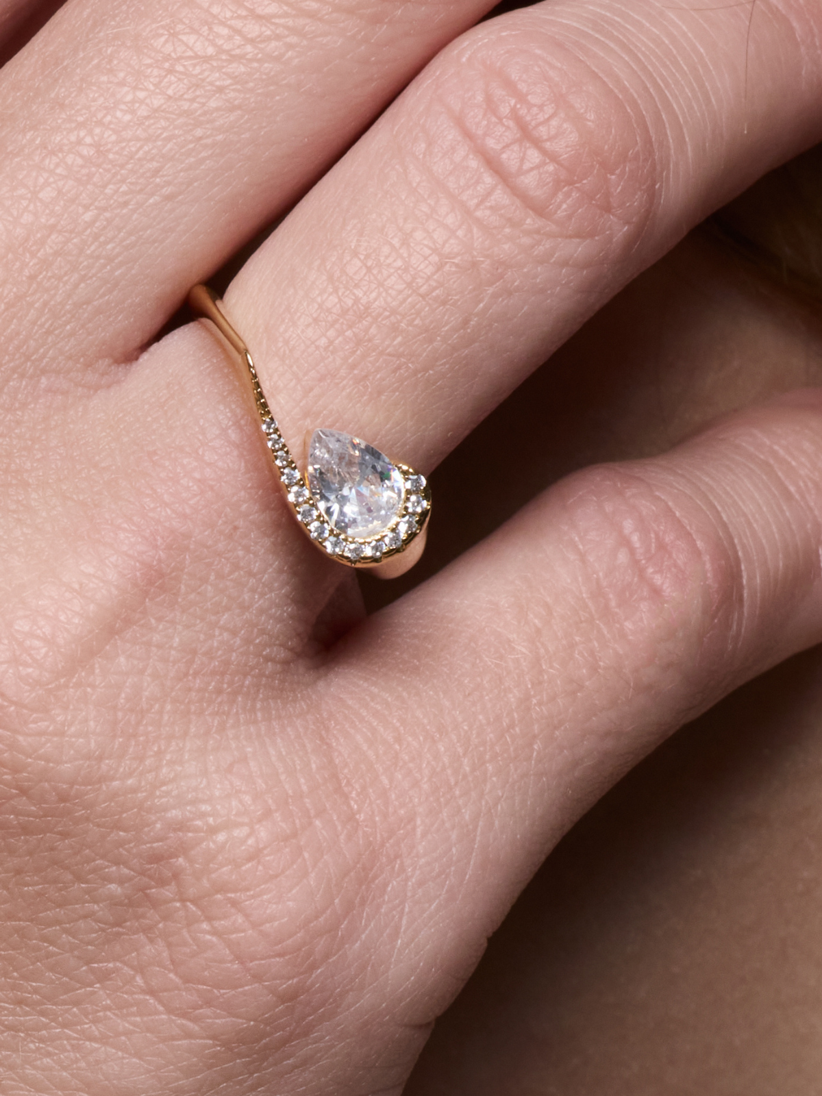 Bague « Pear Glow » en argent 925 rhodié, pierre centrale en zirconium taille poire entourée d’un délicat pavage de zirconiums, anneau légèrement torsadé à la finition polie brillante.