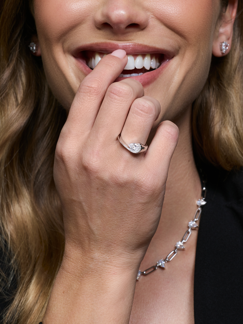 Bague Pear Glow blanche en argent 925 rhodié avec pierre centrale en zirconium taille poire entourée d’un délicat pavage de zirconiums, design fluide et asymétrique qui épouse le doigt pour un éclat subtil et raffiné.