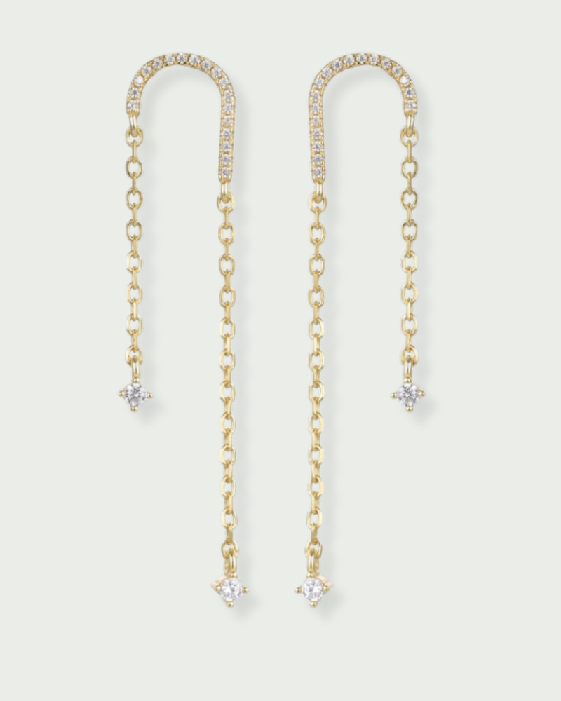 Boucles asymétriques en argent 925 doré à l'or 18 carats, arc pavé de zirconiums et fines chaînes terminées par des pendants en pierres blanches.
