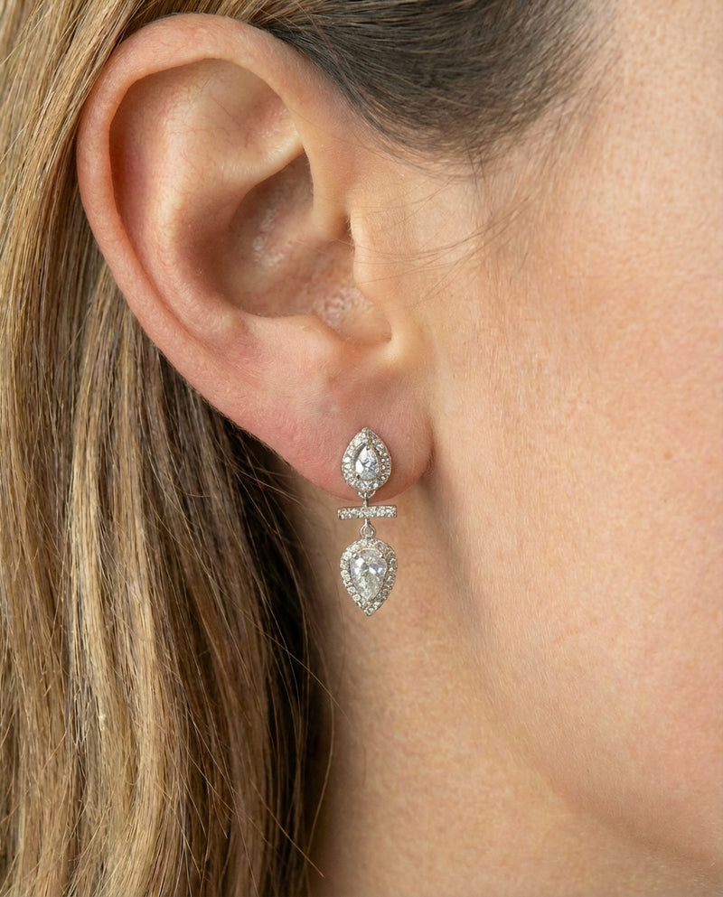 Boucles d’oreilles « Opposite Infini Poire » en argent 925 rhodié, deux zircons blancs taille poire montés en symétrie miroir, séparés par une petite barre sertie, finition polie brillante.