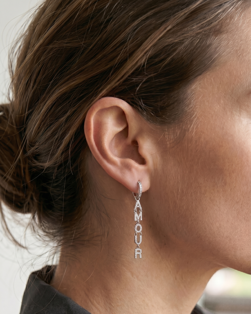Boucles d’oreilles pendantes « Amour » en argent 925 rhodié, lettres serties de zirconiums formant le mot AMOUR suspendues à un anneau, finition polie brillante.