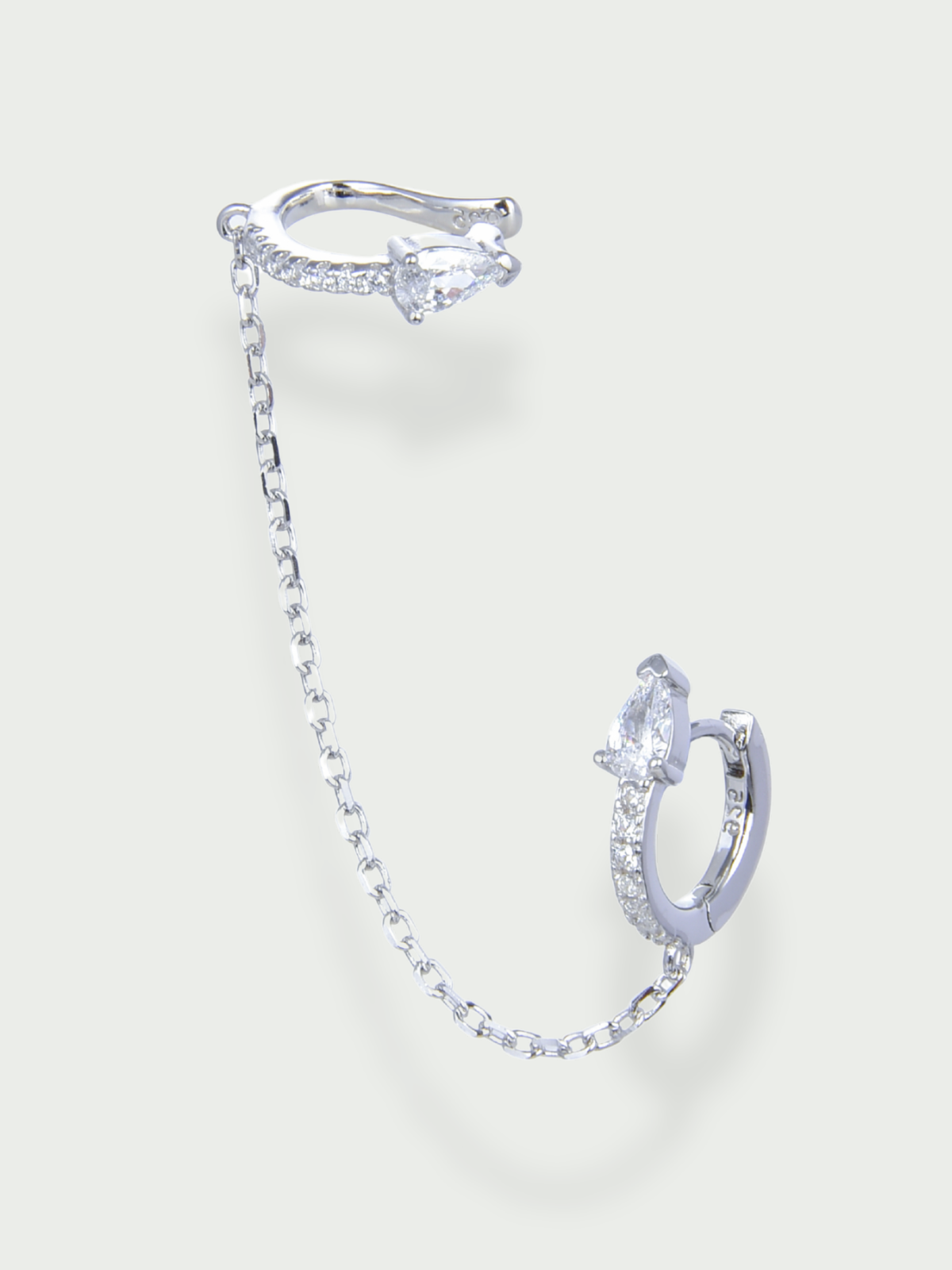 Earcuff Pear Glow blanc en argent 925 rhodié, earcuff et petite créole reliés par une chaîne délicate ornée de zirconiums taille poire, design moderne et lumineux qui habille élégamment l’oreille.