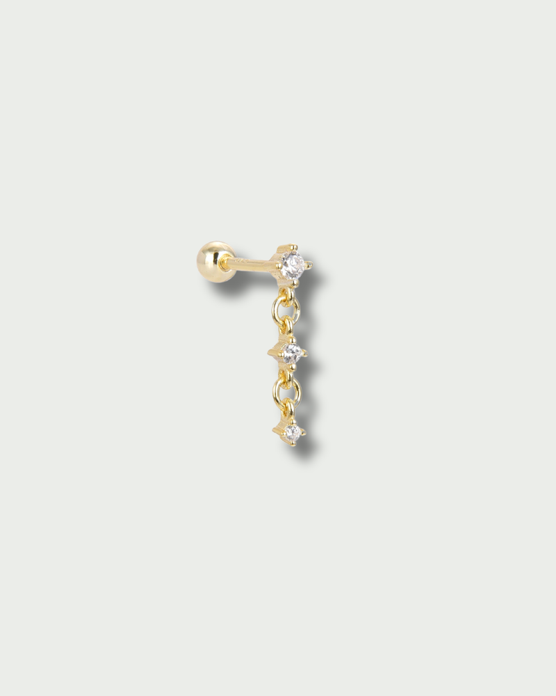 Piercing d’oreille en argent 925 millièmes doré à l’or fin 18 carats, sublimé par trois petites pierres en zirconium délicatement montées sur une fine chaîne. Un design aérien et lumineux qui crée un subtil mouvement à chaque geste.
